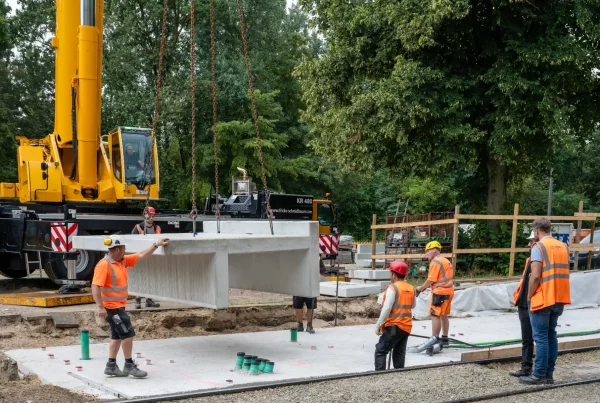 Baustellenansicht an der Haltestelle Reiterstadion, wo ein Kran 8 Tonnen schwere Betonteile von einem Tieflader für den künftigen Hochbahnsteig ablädt.