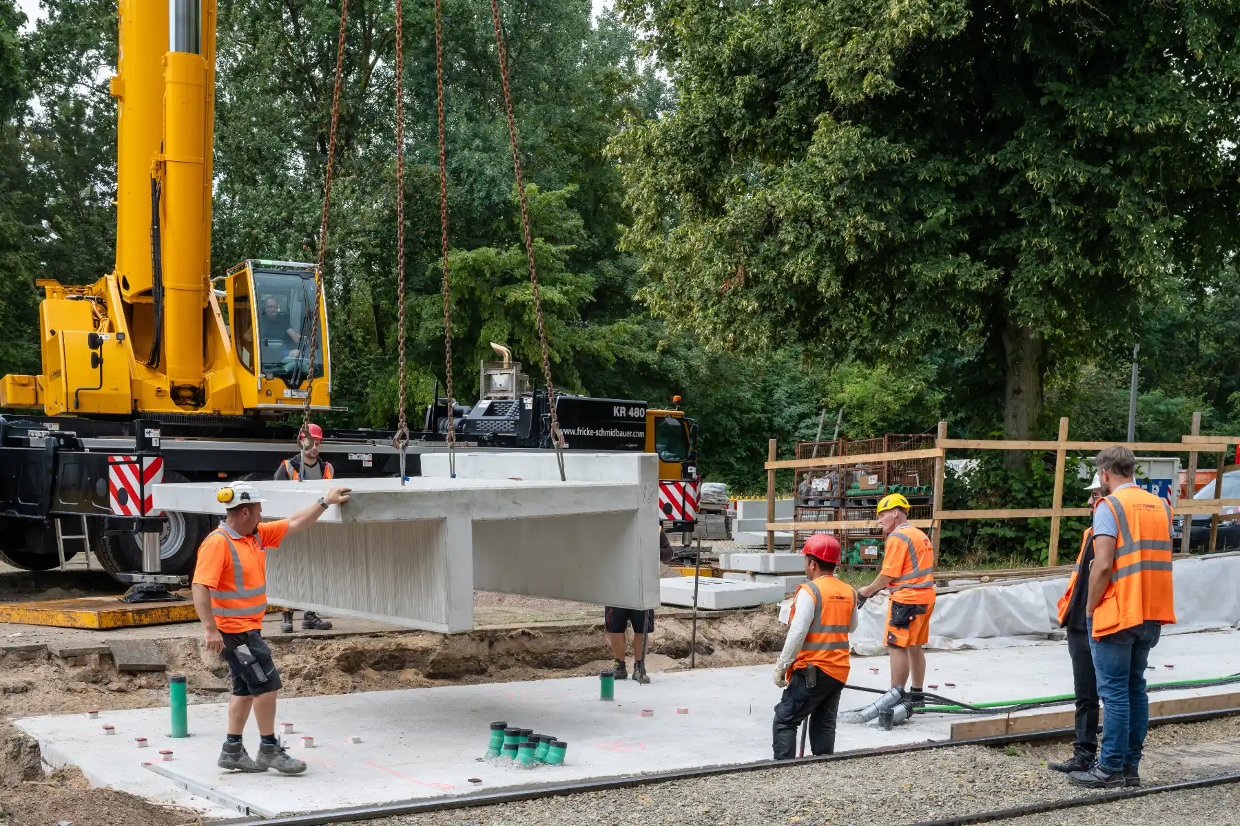 Baustellenansicht an der Haltestelle Reiterstadion, wo ein Kran 8 Tonnen schwere Betonteile von einem Tieflader für den künftigen Hochbahnsteig ablädt.
