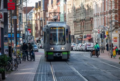 Stark abgenutzte, in das Pflaster eingebettete Stadtbahngleise in der Fußgängerzone der Limmerstraße in Hannover-Linden mit vorbeirollendem Straßen- und Radverkehr.